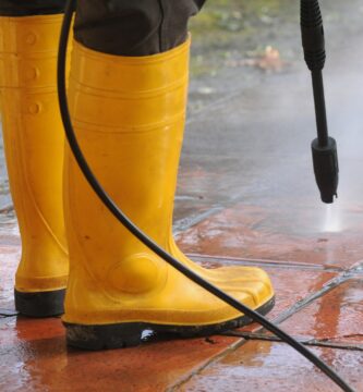 persona vestida botas goma amarilla boquilla agua alta presion limpiando suciedad baldosas